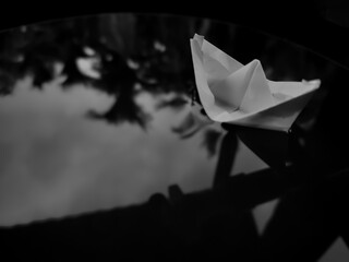 closeup of paper boat floating on water with reflection of trees on water