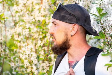 Portrait of Man with Beard in Baseball Cap Against White Flowery Tree in Spring.