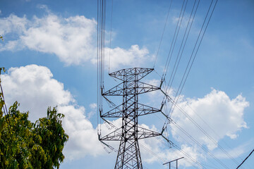 Power lines traverse a sky filled with fluffy white clouds, contrasting with the steel structure of...