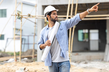 Foreman, engineer, or architect with safety helmet holding laptop and blueprints for inspection details on construction in a new real estate construction site with crane and mechanical equipments.