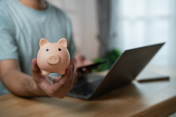 Person Holding Piggy Bank in Front of Laptop for Online Banking and Financial Management in Modern...