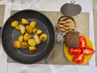 Bachelor dinner of homemade food. Lunch of fried potatoes in a pan, tomatoes and canned sprats.