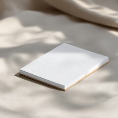 A grid-patterned notepad rests on a beige, softly lit fabric surface with gentle shadows.