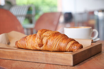Delicious croissant with coffee on a wooden tray in cafe