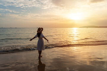 Young Asian woman traveler enjoying beautiful Sunset on the tranquil beach, Travel on summer vacation concept