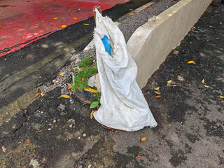 A discarded white woven bag lies on a weathered surface, showcasing textures of concrete and fallen...