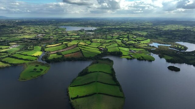 Lough Muckno, County Monaghan, Ireland, September 2022. Drone panoramic high angle pullback across peninsula island with organized hedge rows separating grassy fields under cloudy sky.