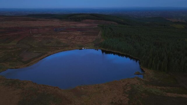 Bragan, County Monaghan, Ireland, September 2022. Drone orbit clockwise medium establishing of Lake Menish and surround bog wetlands with dense patch of forest on single edge.