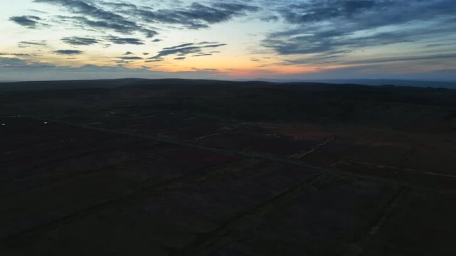 Bragan, County Monaghan, Ireland, September 2022. Drone tracking left follows along road with bog wetlands and peat fields at blue hour dusk, natural backdrop background.