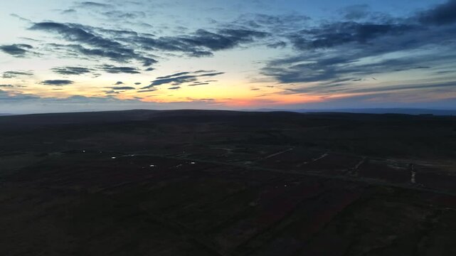 Bragan, County Monaghan, Ireland, September 2022. Drone panoramic aerial orbit counter clock wise over bog wetlands and peat fields with yellow orange sky at blue hour dusk twilight.