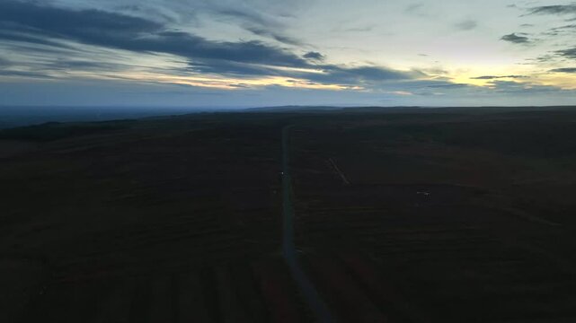 Bragan, County Monaghan, Ireland, September 2022. Drone pullback along road separating peat wetland fields with bog landscape at dusk twilight.