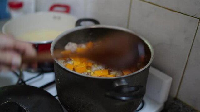 Cook slowly stirs steaming argentina's locro in heavy pot revealing chunks of butternut pumpkin, chorizo sausage, onions, corn kernels simmering in rich stock, aromas rising in a rustic home kitchen