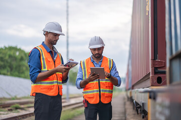Engineers holding detail under survey and checking containers and industrial railway truck machinery in yard is logistic import and export industry concept.