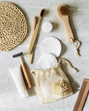 Hygiene products as bamboo toothbrushes, toothpaste, reusable pads, safety razor on grey marble background with natural light, eco-friendly items for self care, zero waste concept. Minimal top view