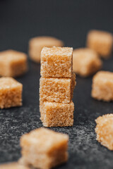 Brown sugar cubes stacked on a dark surface with scattered pieces around