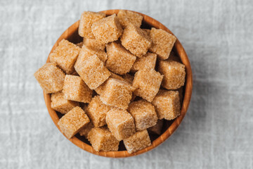 Sugar cubes arranged in a wooden bowl on a neutral surface