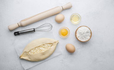 Raw khachapuri with egg yolk and cheese on white background with ingredients