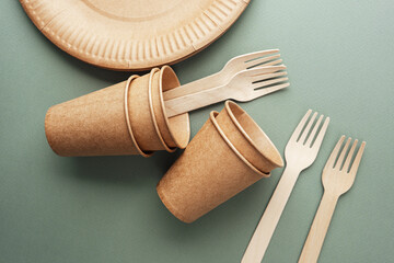 Disposable eco paper cups and wooden forks on green background flat lay view