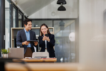 Team of Young business Asian man and woman using using tablet computer standing near the window in workplace	