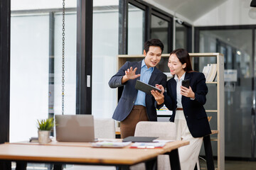Team of Young business Asian man and woman using using tablet computer standing near the window in workplace	