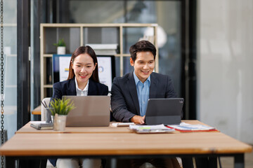 Young Asian Man and Woman manager project on laptop in modern office. Two business people of professional working, studying, writing notes sit at desk 
