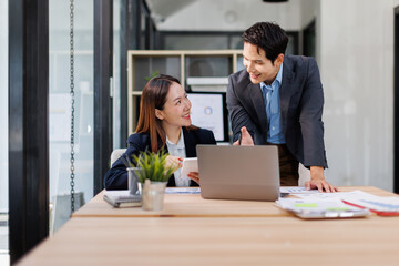 Fototapeta premium Young Asian Man and Woman manager project on laptop in modern office. Two business people of professional working, studying, writing notes sit at desk 