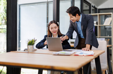 Young Asian Man and Woman manager project on laptop in modern office. Two business people of professional working, studying, writing notes sit at desk 
