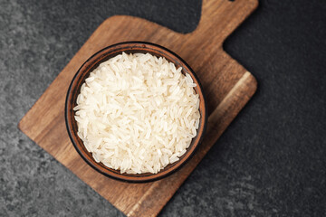 Bowl of uncooked white rice on a wooden cutting board in kitchen