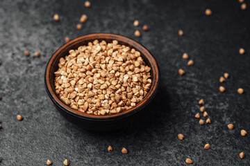 Buckwheat grains in a wooden bowl on a textured dark surface