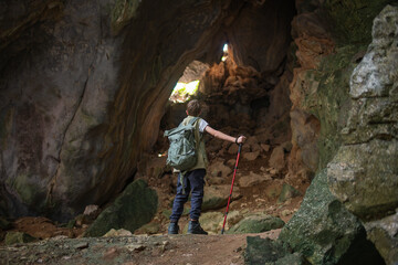 Tourist trekking with backpack and using a walking stick, gesturing forward suggesting of adventure or discovery in cave mysterious and ancient outdoor adventure concept.