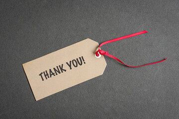 Thank you tag with red ribbon. On top of dark surface. High angle view.