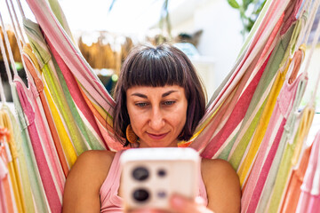 Woman lying in hammock using smartphone. summer mood. girl relaxing swinging in hammock and scrolling social media near summer camping.