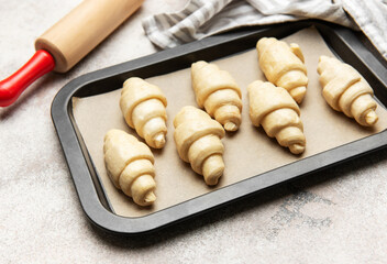 Raw croissants baking on tray with rolling pin and kitchen towel