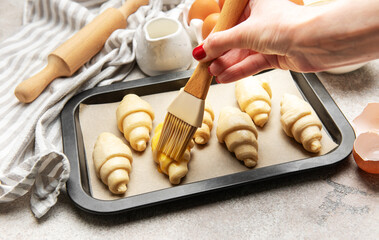 Baker brushing egg yolk on raw croissants on baking sheet