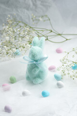 Soft pastel bunny surrounded by candy on a light textured fabric