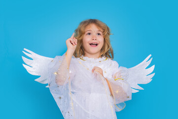 Child angel pointing up, point gesture. Cute angel kid, studio portrait. Blonde curly little angel...