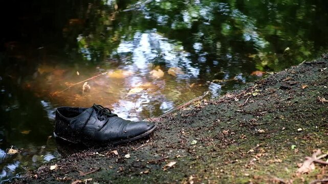 A discarded black shoe lies on the riverbank polluting the water. Environmental problems. Human harm to nature. Discarded garbage is a concept of planet pollution. Criminale story. HQ Full HD footage.