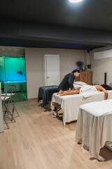 Physiotherapist performing leg massage on patient lying on massage table in modern physiotherapy center with relaxing aquarium