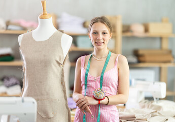 Young female seamstress adjusting clothes on mannequin in sewing workshop