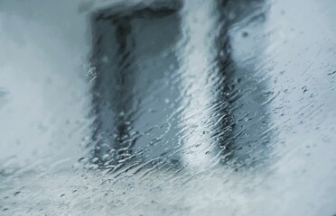 Abstraktes Motiv mit Regenwassermuster auf Glasscheibe vor weißer Hauswand mit Fenster von Wohnhaus in Stadt bei Regen am Abend im Frühling