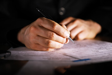 ** Businessperson Signing Document with Pen in Dim Light, Close-Up Office Work