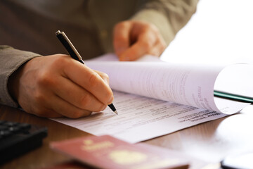 Close-Up of Person Filling Out Forms with Pen and Passport on Wood Table