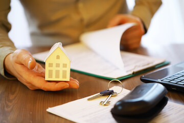 Businessman Holding Miniature House, Reviewing Real Estate Documents and Contracts with House Keys on Desk