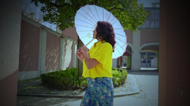 Fashionable young woman holding a pink parasol in a sunny garden setting, enjoying a peaceful moment. 