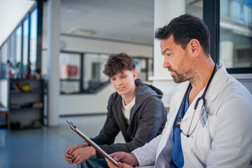 Doctor explaining medical procedure to teenage patient in hospital waiting room.