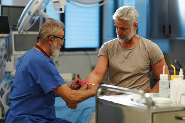 Fototapeta premium Older doctor drawing blood from patient's arm.