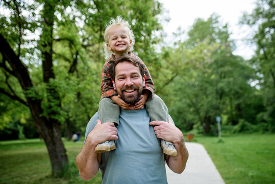 Father carrying his smiling son on shoulders during walk in park