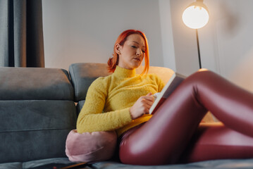Obraz premium Woman relaxing on sofa reading a book and drinking tea