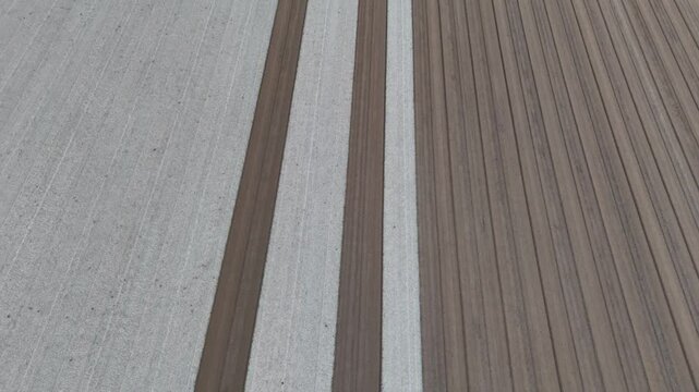 slow-motion drone shot reveals perfectly parallel strips of pale tilth and rich brown earth freshly leveled across a vast field forming an orderly grid poised for the next planting season