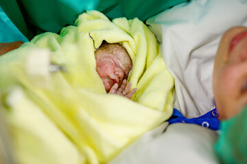 Newborn baby wrapped in blankets after birth. Mother looking for the first time on new born...